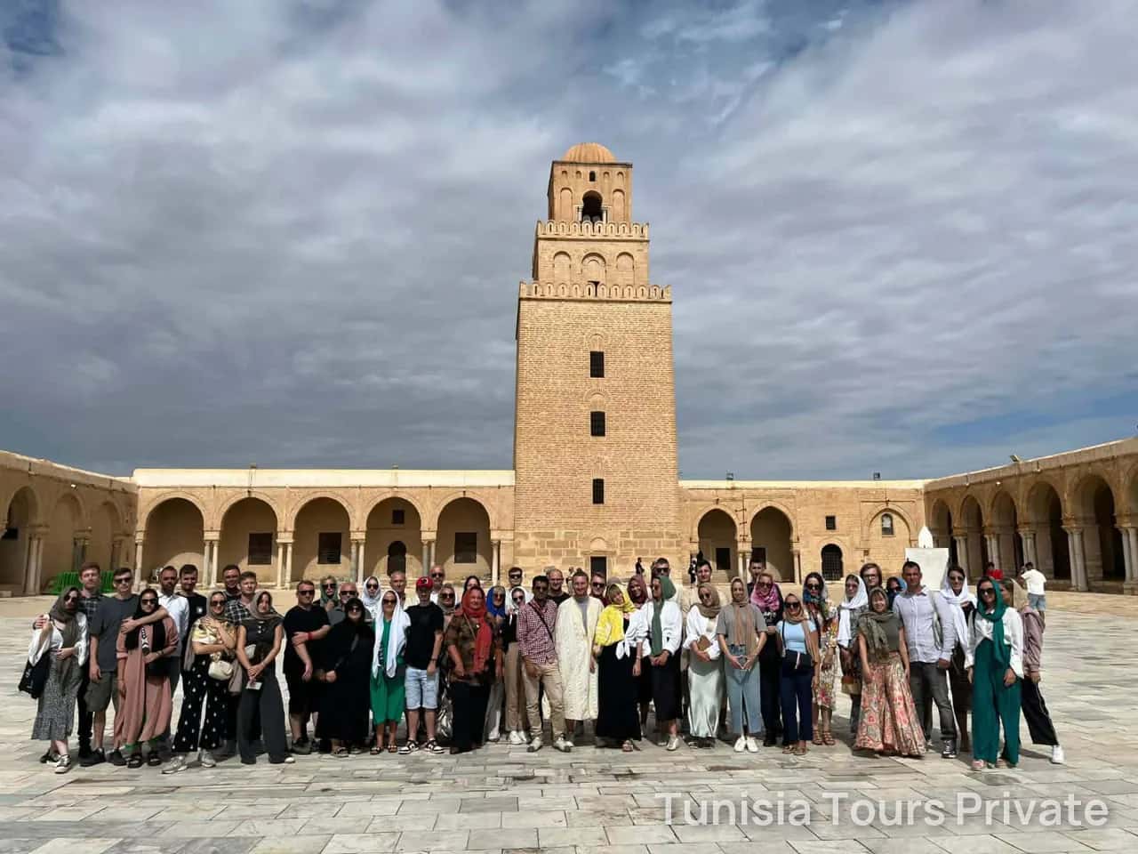 A group gathered in the courtyard of the Great Mosque of Kairouan below its minaret