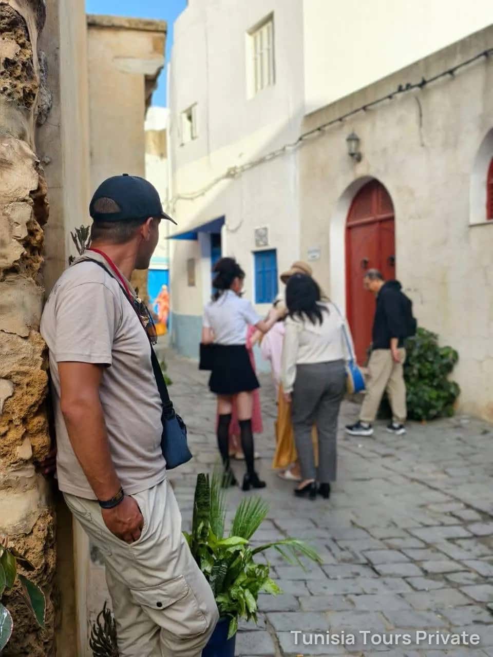 A guide waits for his group in a white medina lane with a red door