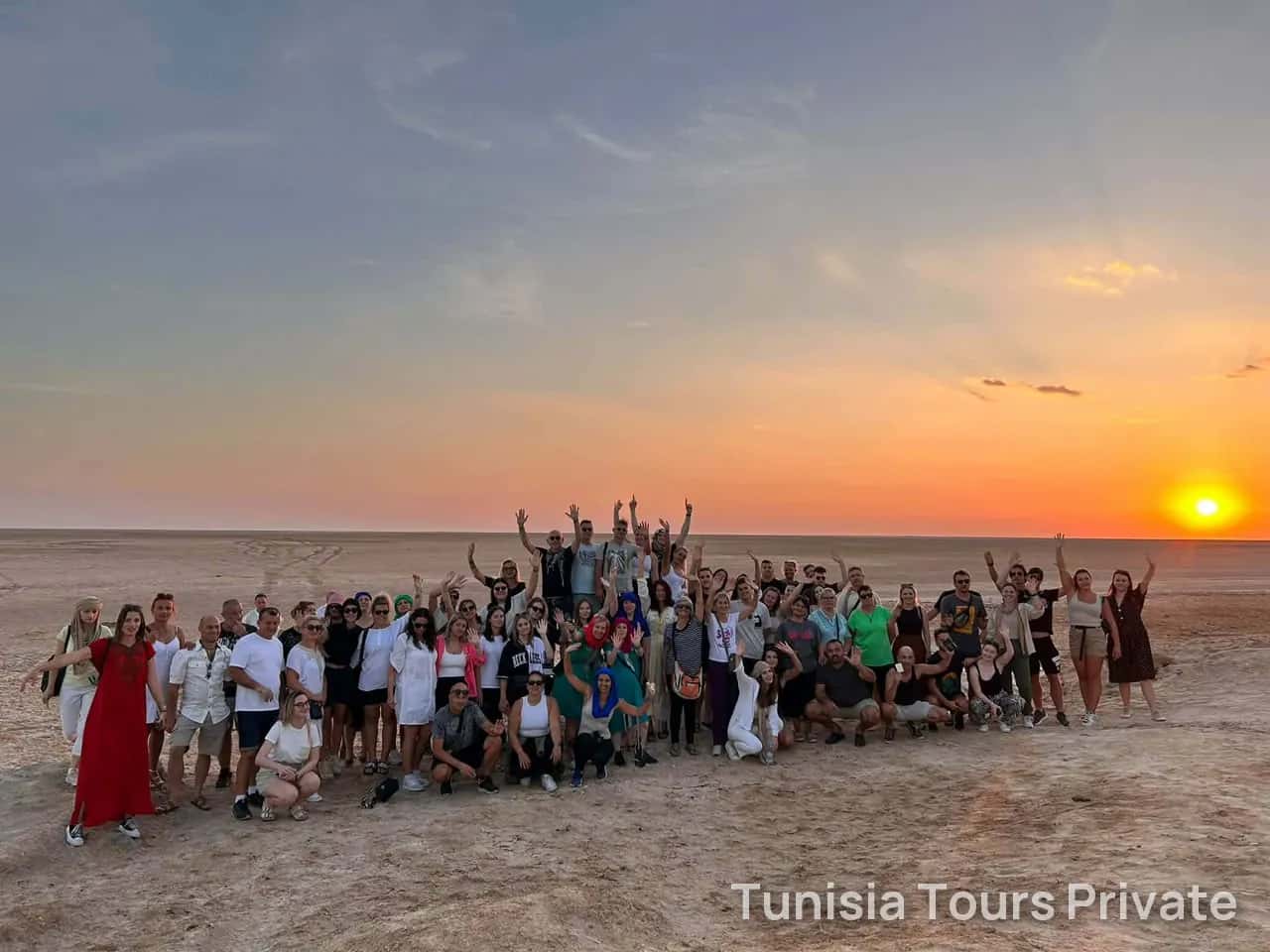 A happy group raising their arms in the desert as the sun sets
