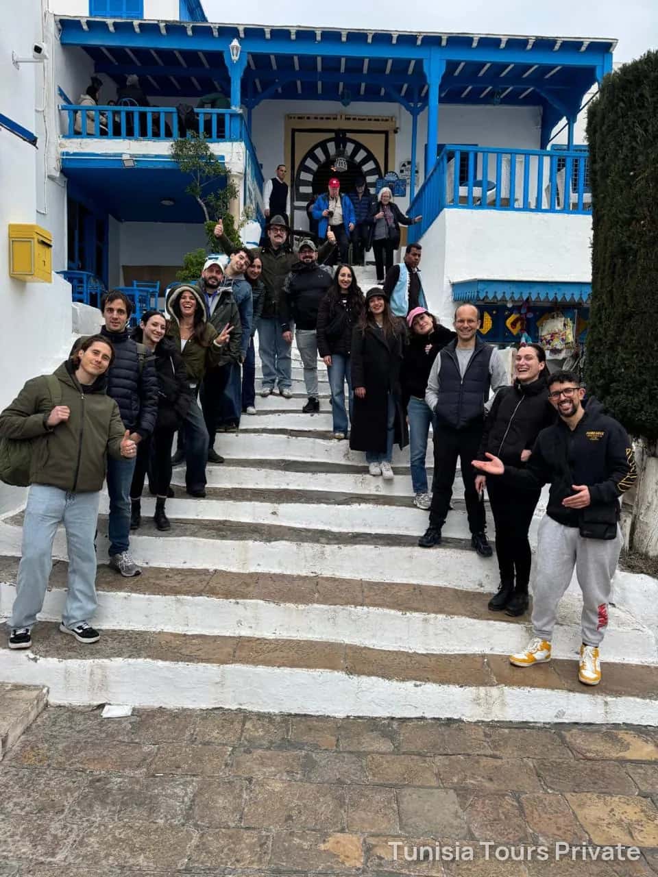 A group on the white steps below a blue café terrace in Sidi Bou Saïd