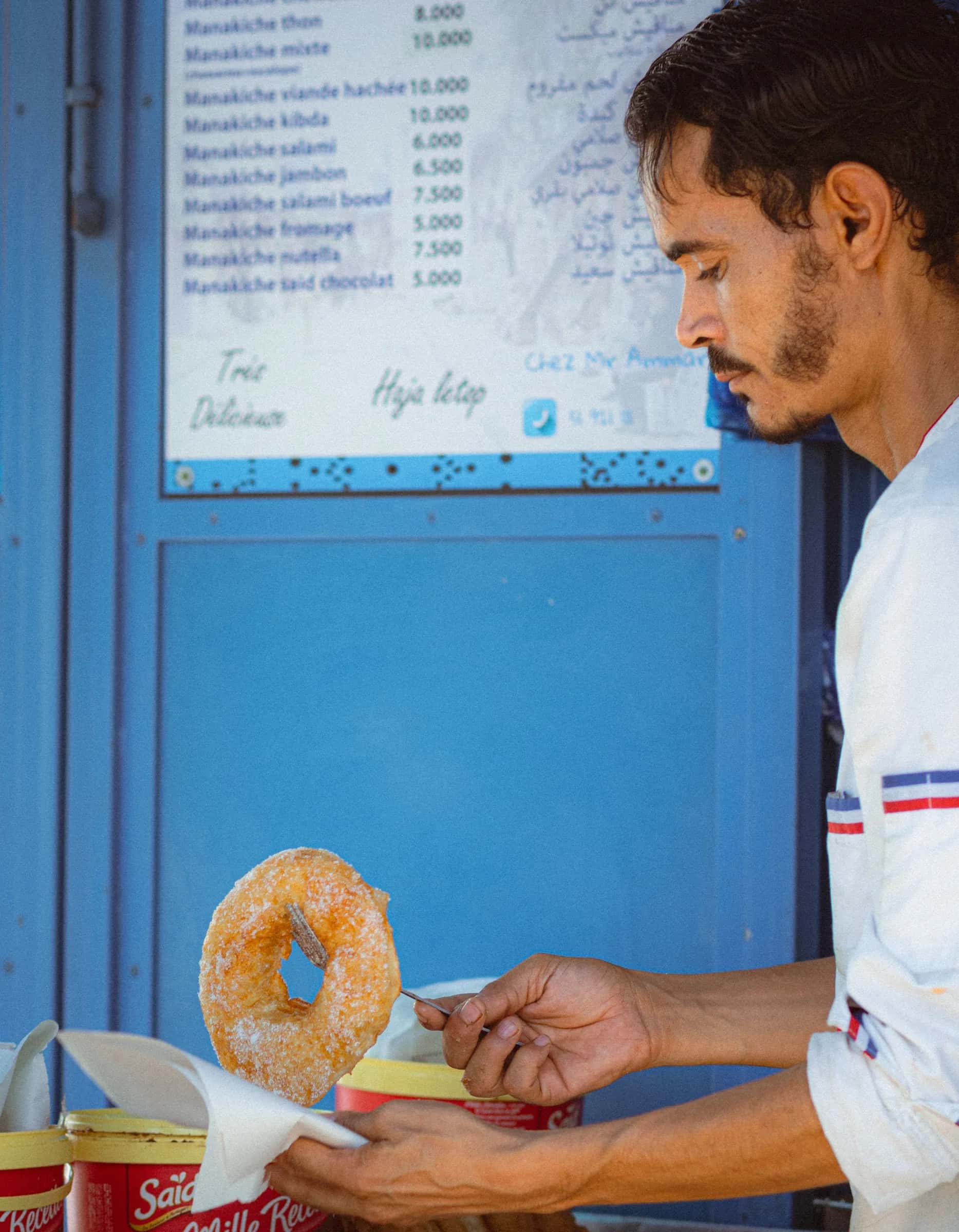 Un vendedor entrega un bambalouni azucarado, el buñuelo tunecino, en un quiosco azul