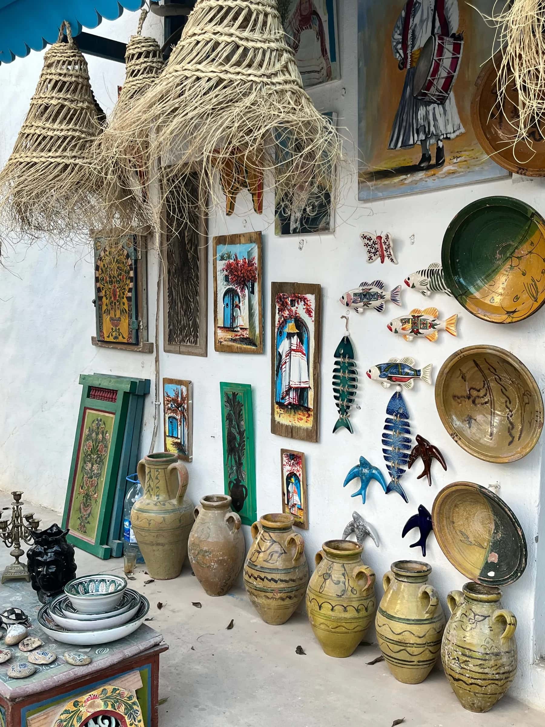 Platos pintados, sombreros de paja y tinajas de barro en la pared de una tienda de artesanía de Djerba