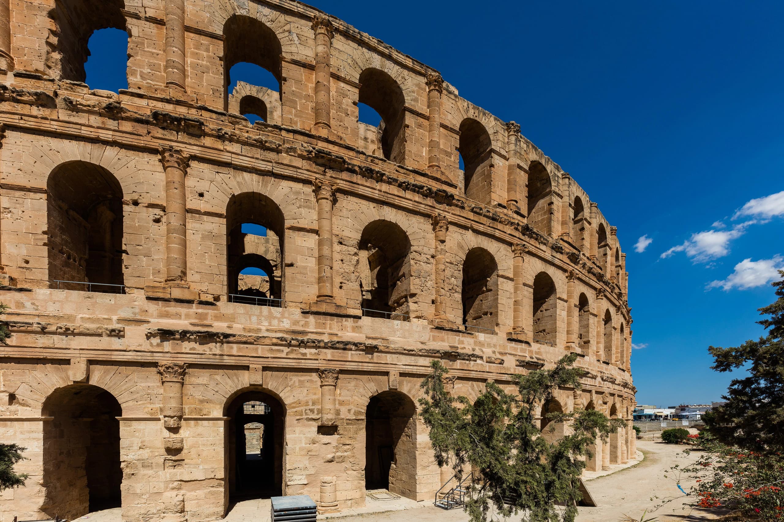 Three tiers of arches on the outer wall of the El Jem amphitheatre under a deep blue sky