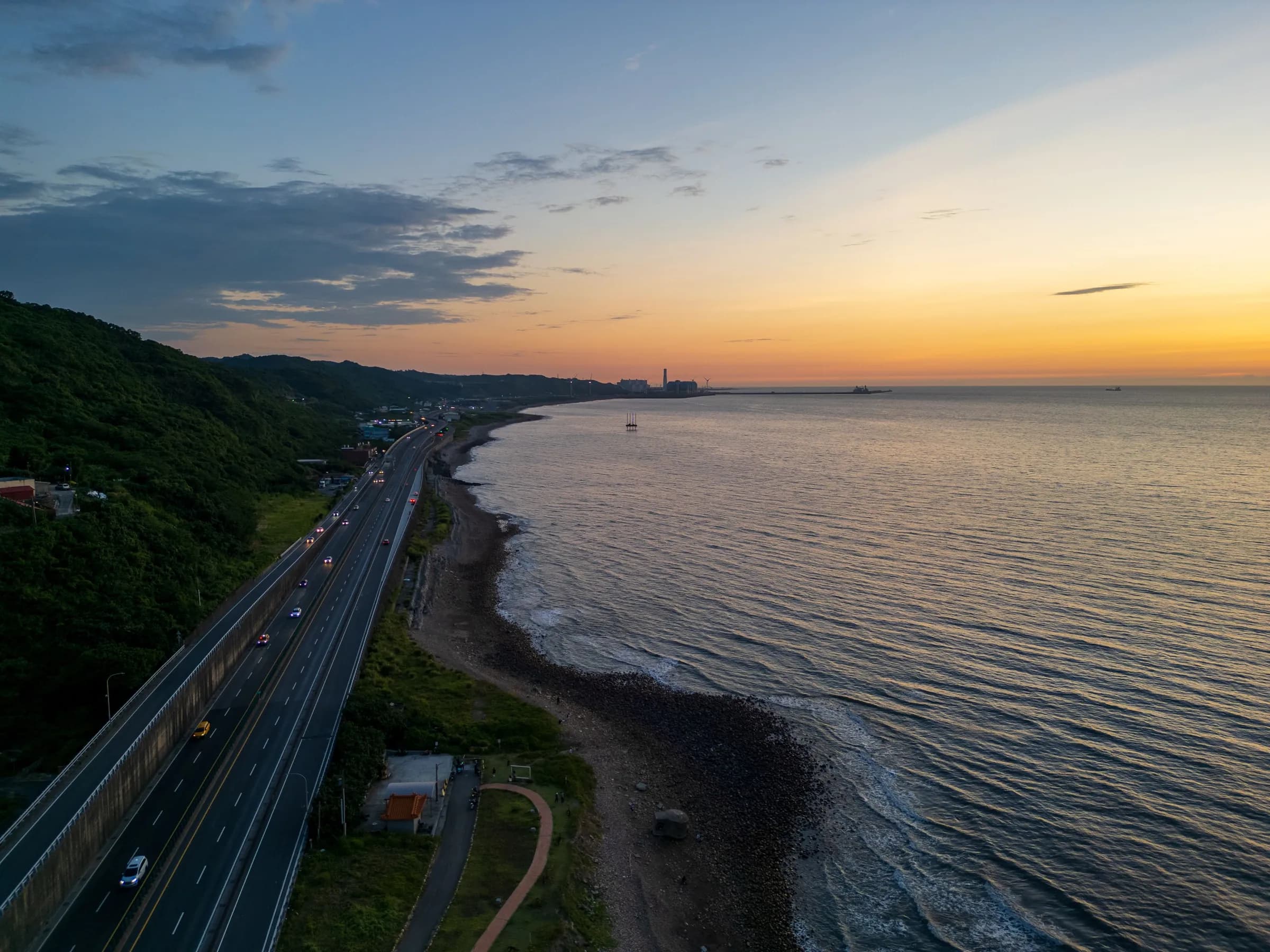 A coastal road running beside the sea under a glowing orange sky at dusk