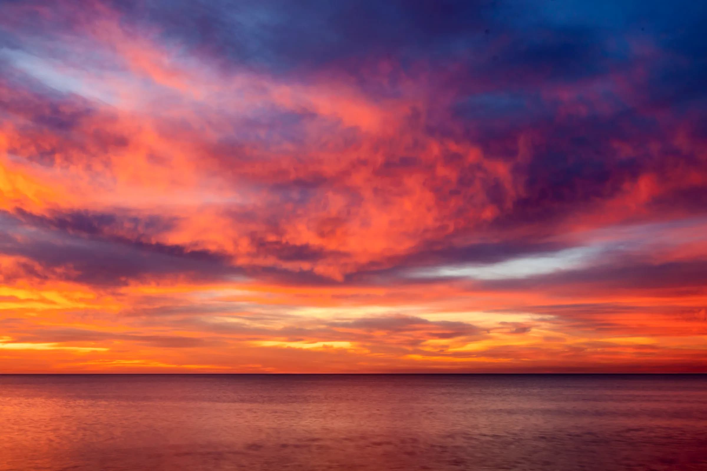 A blazing orange and violet sky over a calm sea at sunset