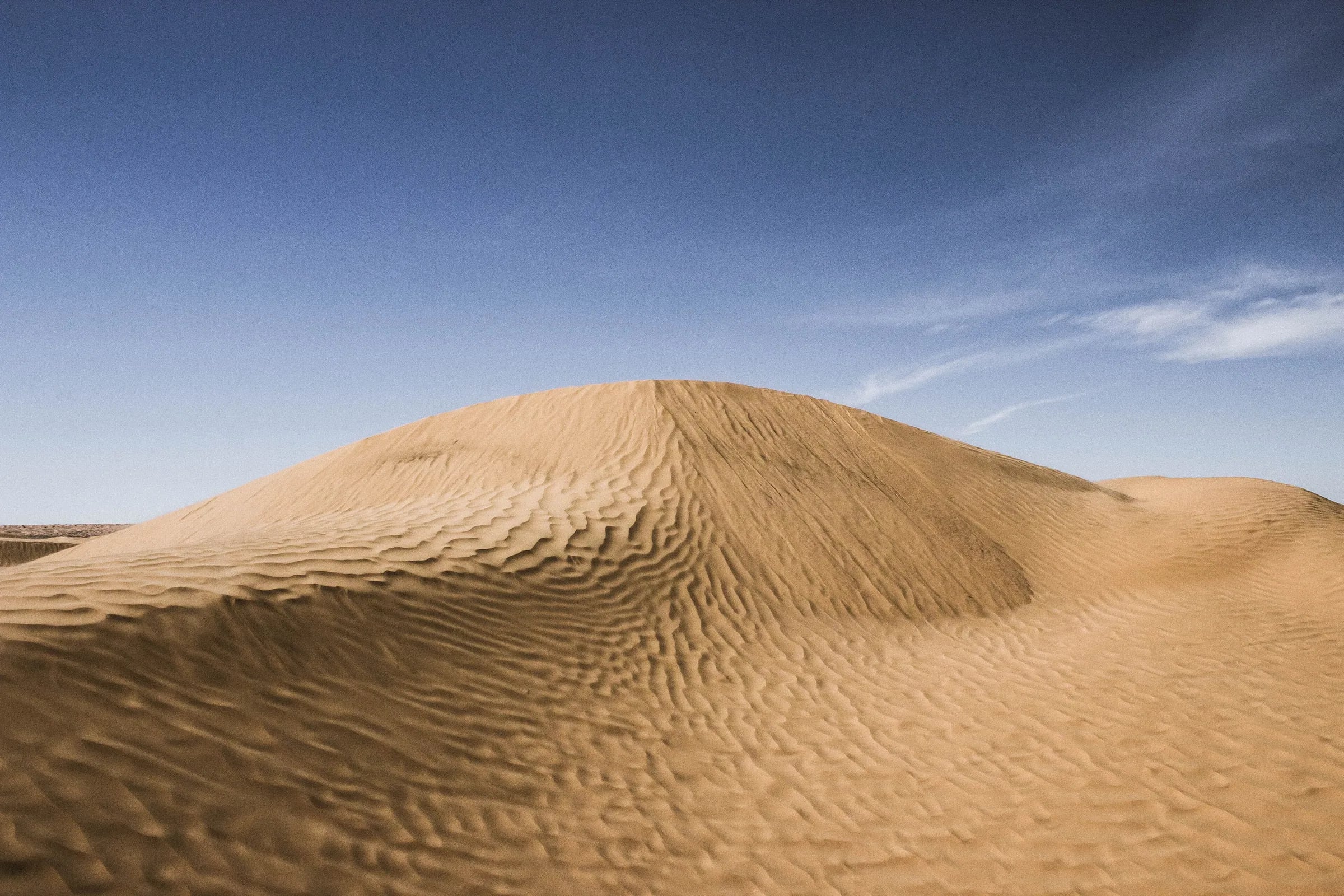 Une dune de sable ridée à Ksar Ghilane sous un ciel bleu
