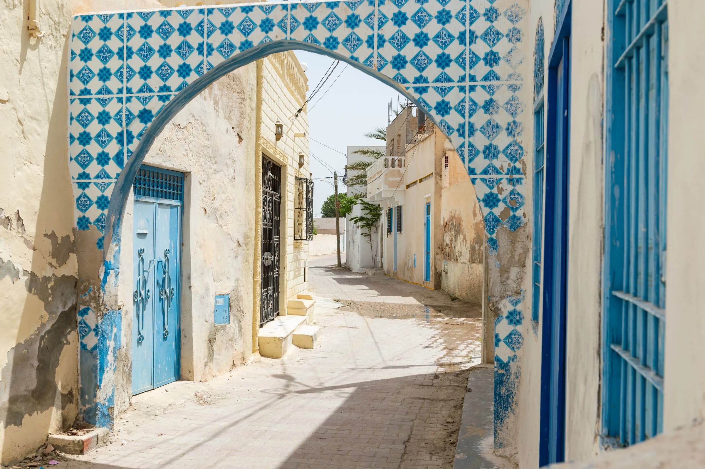 Un arco di piastrelle blu sopra un vicolo bianco a Djerbahood